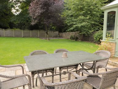 A garden patio with a stone table and six wicker chairs surrounded by grass and trees at Walworth Castle Lodge in Walworth near Darlington