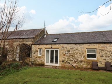A stone cottage with a slate roof and patio doors next to a grassy yard at Christon Well Cottage in Christon Bank near Embleton