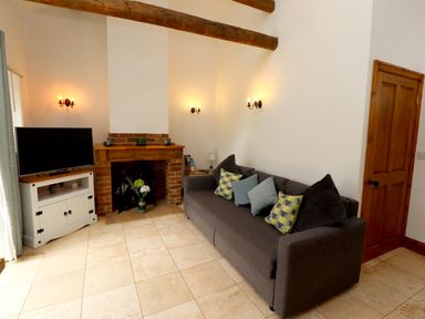 A living room with a gray sofa with pillows a television on a white cabinet and a brick fireplace at Christon Well Cottage Christon Bank near Embleton