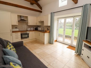 A kitchen living area with cream cabinets tiled floor and glass doors opening to a garden at Christon Well Cottage Christon Bank near Embleton
