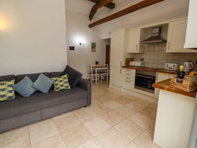A kitchen with white cabinets a gray sofa with patterned cushions and a small dining table with chairs at Christon Well Cottage in Christon Bank near Embleton