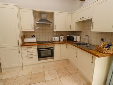 A kitchen with cream cabinets wooden countertops oven stove microwave kettle toaster and a sink at Christon Well Cottage Christon Bank near Embleton