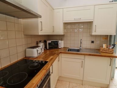 A kitchen with wooden countertops a sink a microwave a toaster and cream colored cabinets at Christon Well Cottage in Christon Bank near Embleton