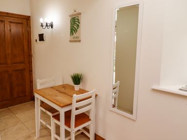 A small wooden table with two white chairs a potted plant on the table a wall mirror and a wooden door at Christon Well Cottage Christon Bank near Embleton