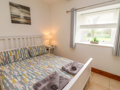 A bedroom with a bed with patterned bedding bedside table with lamp window with blinds and curtains painting on wall at Christon Well Cottage Christon Bank near Embleton