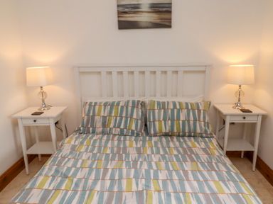 A bedroom with a bed with patterned bedding two bedside tables each with a lamp and a picture on the wall above at Christon Well Cottage in Christon Bank near Embleton