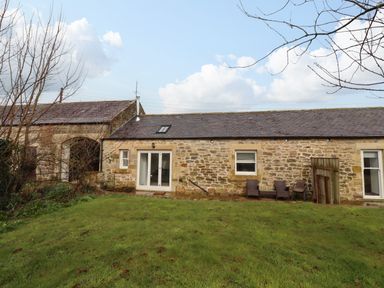 A stone cottage with sliding glass doors and two chairs in a grassy garden at Christon Well Cottage in Christon Bank near Embleton