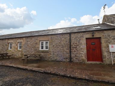 A stone cottage exterior with a red door and two wooden picnic tables at Christon Well Cottage Christon Bank near Embleton