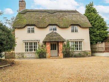 A thatched roof cottage with brick porch and multiple windows surrounded by trees at Moles Cottage in Farnham near Sixpenny Handley