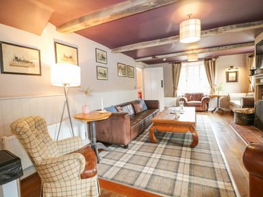 A living room with a brown leather sofa a plaid armchair wooden table and a fireplace at Moles Cottage Farnham near Sixpenny Handley