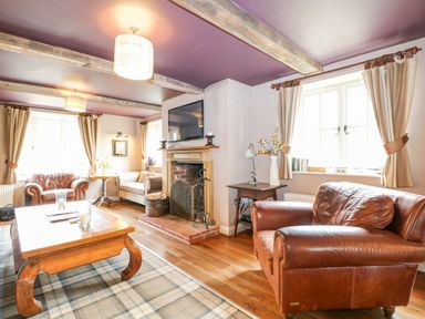 A living room with leather armchairs a wooden coffee table fireplace and a mounted television at Moles Cottage Farnham near Sixpenny Handley