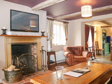 A living room with a fireplace a leather armchair a wooden coffee table and a mounted television at Moles Cottage in Farnham near Sixpenny Handley