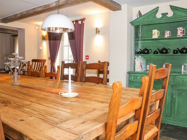 A dining room with a long wooden table and wooden chairs a green cabinet with dishes and cups and purple curtains at Moles Cottage Farnham near Sixpenny Handley