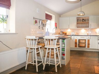 A kitchen with white cabinets two white bar stools and utensils hanging on the wall at Moles Cottage Farnham near Sixpenny Handley