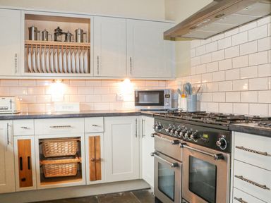 A kitchen with white cabinets a black stove a microwave a toaster and plates stored in an upper cabinet at Moles Cottage Farnham near Sixpenny Handley