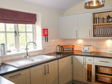 A kitchen with a sink under a window a kettle a toaster and dishes on shelves at Moles Cottage in Farnham near Sixpenny Handley