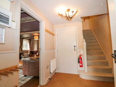 A hallway with carpeted stairs a closed door a fire extinguisher and a glimpse of a living room at Moles Cottage in Farnham near Sixpenny Handley