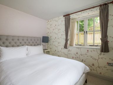 A bedroom with a bed table lamp and window with curtains at Moles Cottage Farnham near Sixpenny Handley