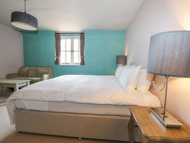 A bedroom with a large bed white bedding a lamp on a wooden bedside table a window with curtains a sofa and a coffee table at Moles Cottage Farnham near Sixpenny Handley