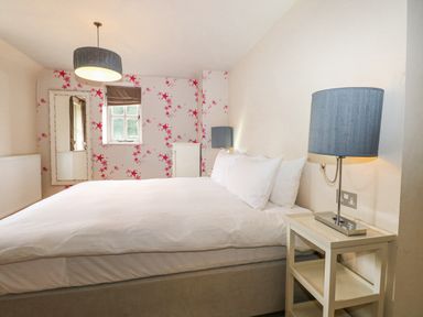 A bedroom with a large bed white bedding a bedside table with a lamp a window and a full length mirror at Moles Cottage Farnham near Sixpenny Handley