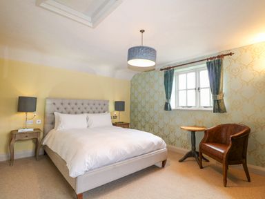 A bedroom with a double bed two bedside tables with lamps a window with curtains a round table and a leather chair at Moles Cottage in Farnham near Sixpenny Handley
