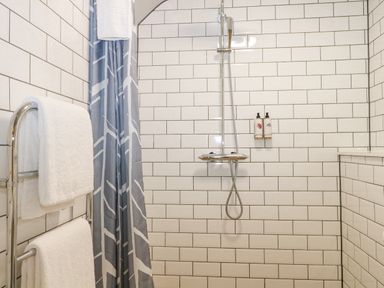 A tiled shower area with a handheld showerhead two wall-mounted bottles and towels on a rack at Moles Cottage Farnham near Sixpenny Handley