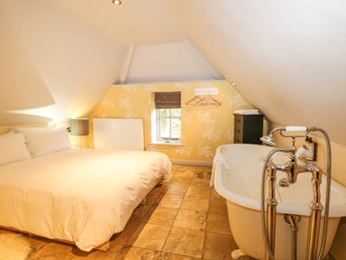 A bedroom with a bed, a bathtub, a small window, and a chest of drawers at Moles Cottage in Farnham near Sixpenny Handley