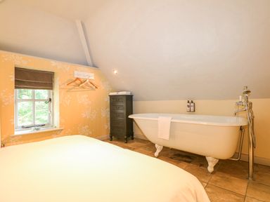 A bedroom with a clawfoot bathtub a chest of drawers and a window at Moles Cottage in Farnham near Sixpenny Handley