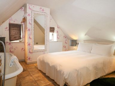 A bedroom with a large bed white bedding a floor mirror and a bathtub at Moles Cottage in Farnham near Sixpenny Handley
