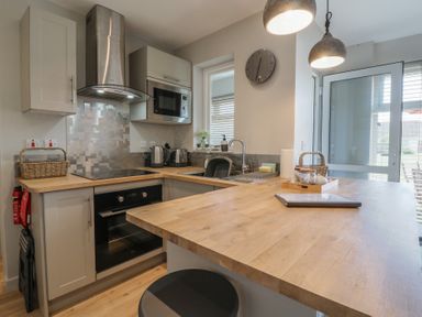 A kitchen with wooden countertops a black oven a microwave a sink and hanging lights at 1 Kessingland Cottages in Kessingland