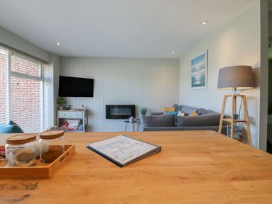 A living room with a grey sofa a wall-mounted tv a small table with board games and a wooden lamp at 1 Kessingland Cottages in Kessingland