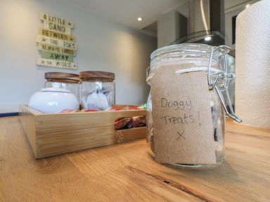 A kitchen countertop with a jar labeled Doggy Treats a wooden tray with containers and paper towels at 1 Kessingland Cottages in Kessingland