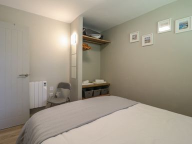 A bedroom with a bed a chair an open closet with hangers baskets and folded towels and framed pictures on the wall at 1 Kessingland Cottages in Kessingland