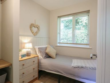 A bedroom with a single bed a bedside table with a lamp and a heart-shaped wall decoration at 1 Kessingland Cottages in Kessingland