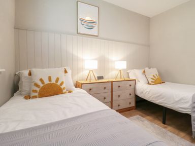 A bedroom with two single beds each with a sun design pillow and a wooden twin dresser with lamps between the beds at 1 Kessingland Cottages in Kessingland