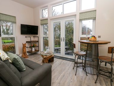 A living room with a sofa table a mounted television and a round dining table with chairs at Elderflower Lodge in Allithwaite near Cartmel