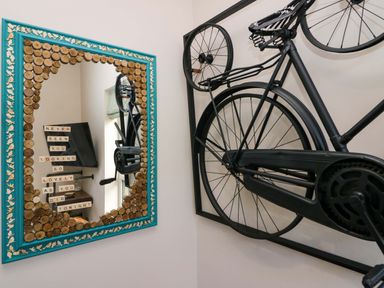 A black bicycle mounted on a wall next to a mirror with a decorative turquoise and wood frame and a message at Elderflower Lodge in Allithwaite near Cartmel