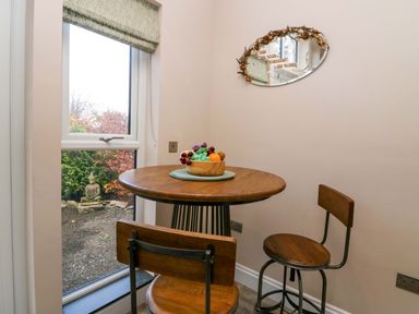 A small dining area with a round wooden table and two wooden chairs beside a window at Elderflower Lodge in Allithwaite near Cartmel