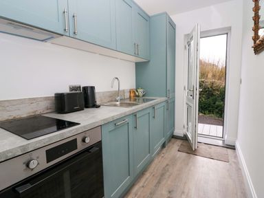 A kitchen with blue cabinets a sink an oven toaster kettle and an open door to the outside at Elderflower Lodge in Allithwaite near Cartmel