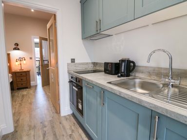 A kitchen with blue cabinets a sink a kettle and toaster next to an open door leading to a bedroom at Elderflower Lodge in Allithwaite near Cartmel
