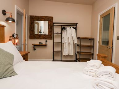 A bedroom with a bed folded towels on the bed a wooden mirror three bathrobes hanging on a rack and wooden shelves at Elderflower Lodge in Allithwaite near Cartmel