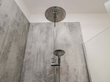A shower area with a rain showerhead and handheld showerhead against gray tiled walls at Elderflower Lodge in Allithwaite near Cartmel