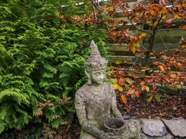 A stone statue of a person holding a bowl in a garden with green and orange foliage at Elderflower Lodge in Allithwaite near Cartmel