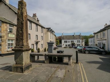 A street view with stone steps and an old stone pillar near buildings including a bookstore and a pub called Kings Arms in a village