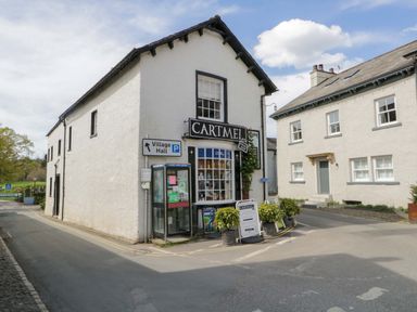 A street corner with a white building labeled Cartmel village shop and a phone booth at Elderflower Lodge in Allithwaite near Cartmel