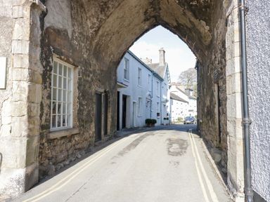 A narrow street passing under an old stone arch with white houses and a car in the background at Elderflower Lodge in Allithwaite near Cartmel