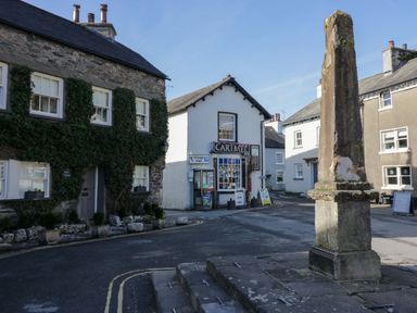 A street corner with stone buildings a shop with cartmel sign and a stone monument at Elderflower Lodge in Allithwaite near Cartmel