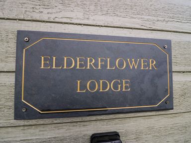 A sign with the text Elderflower Lodge mounted on a wooden wall at Elderflower Lodge in Allithwaite near Cartmel