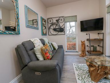 A living room with a gray sofa cushions mirrored wall decor a television and a wooden coffee table at Elderflower Lodge in Allithwaite near Cartmel