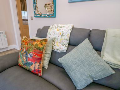 A grey sofa with patterned cushions and folded blankets in a living room at Elderflower Lodge in Allithwaite near Cartmel